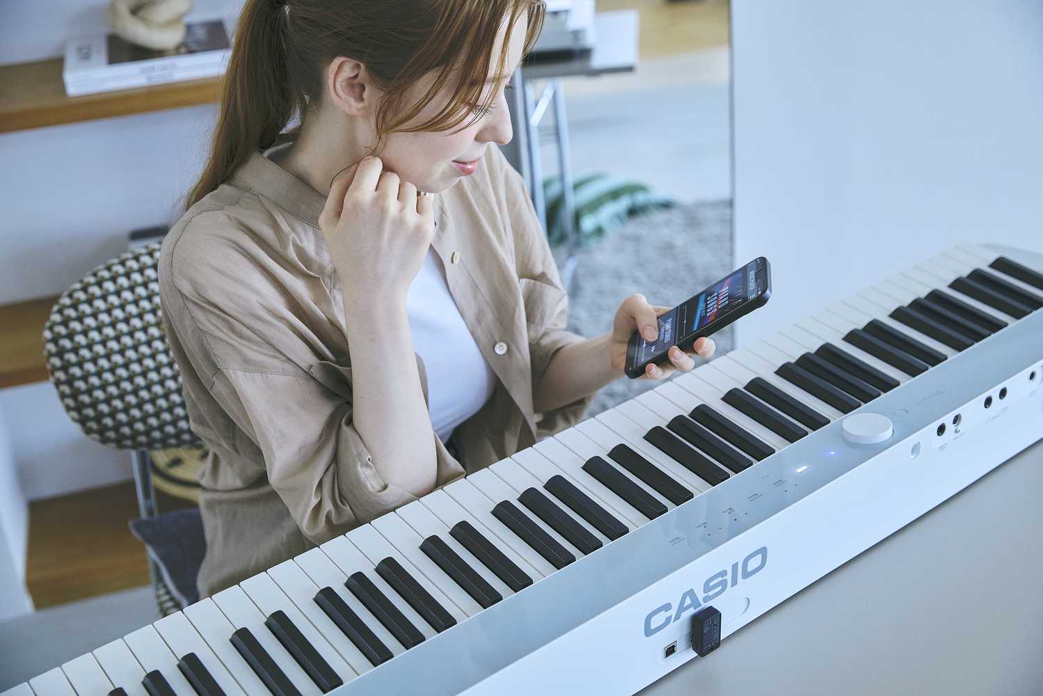 Casio Privia PX-S1100CB Lifestyle Frau mit Smartphone sitzt beim Piano